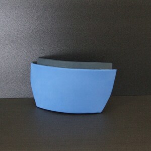 Op de afbeelding: Een gebogen schuimobject in blauw en zwart. Het object bestaat uit twee delen schuim, een blauw en een zwart. Het blauwe schuim bevindt zich aan de onderkant en het zwarte schuim aan de bovenkant.