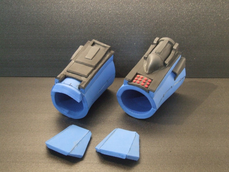 Op de afbeelding: Twee blauwe en zwarte foam polsmanchetten met een klein rood knopje paneel op een manchet. Twee extra blauwe foam stukken zijn ook inbegrepen.