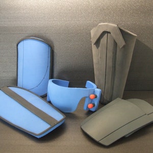 Op de afbeelding: Vijf schuimstukken voor het maken van cosplay of kostuums. Twee zijn blauw met zwarte bies, &eacute;&eacute;n is blauw met rode accenten en twee zijn zwart.