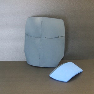 May include: Two pieces of foam, one is a large, dark blue, rectangular piece with lines drawn on it, the other is a smaller, light blue, curved piece.