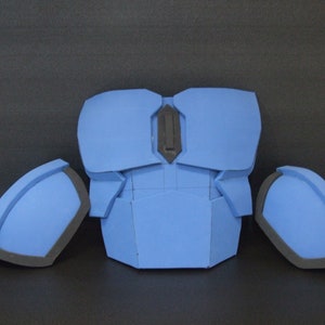 Può includere: Un pezzo per il petto di un costume in schiuma blu con due spalline abbinate. Il pezzo per il petto ha un dettaglio nero al centro e le spalline hanno un bordo nero.