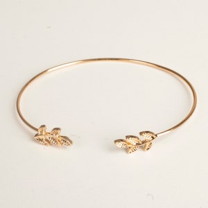 May include: A gold-toned bangle bracelet with a delicate leaf design on each end.