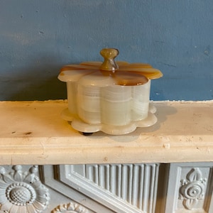 Może przedstawiać: Biało-brązowa alabastrowa szkatułka na drobiazgi w kształcie kwiatu z zaokrągloną pokrywką. Szkatułka stoi na białym tle z ozdobnymi rzeźbami kwiatowymi.