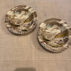 May include: Two brown and white ceramic bowls with a cottage scene design. The bowls have a scalloped edge and a raised rim.