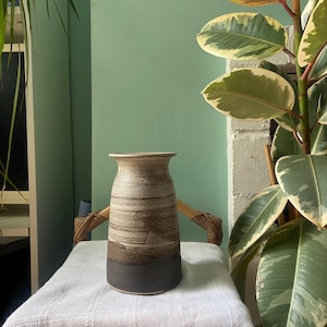 以下が含まれることがあります： 茶色と白のセラミック製の壺で、底の部分は濃い茶色の釉薬がかかっています。壺は白いテーブルクロスの上に置かれています。
