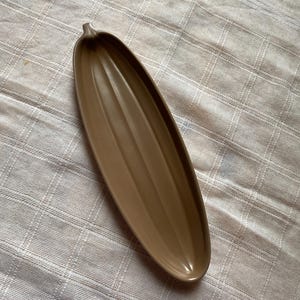 Puede incluir: Un plato de servir de cerámica marrón con forma de calabaza larga y estrecha. El plato tiene un acabado liso y brillante y es perfecto para servir aperitivos o entrantes.