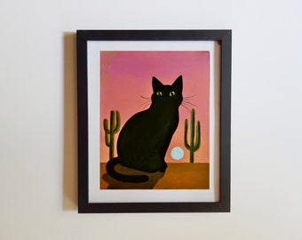 May include: A framed painting of a black cat sitting in a desert landscape with two green cacti and a white moon. The background is a pink sunset.