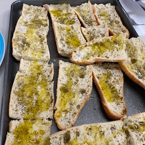 Puede incluir: Una bandeja para hornear llena de rebanadas de pan untadas con aceite de oliva y espolvoreadas con pimienta negra.