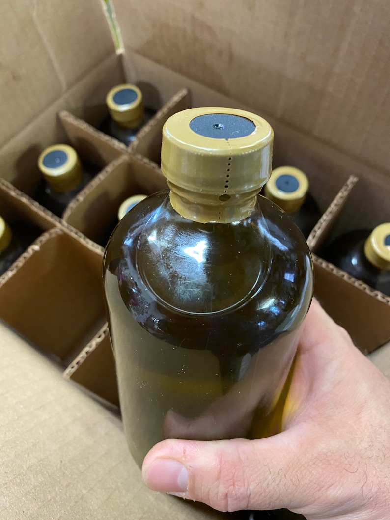 Puede incluir: Primer plano de una botella de vidrio marr&oacute;n con una tapa dorada. La botella est&aacute; en una caja de cart&oacute;n con otras botellas.
