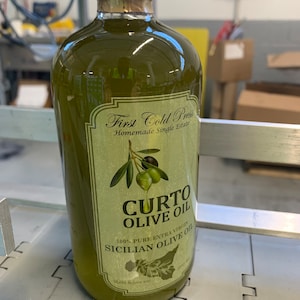 Puede incluir: Una botella de vidrio de aceite de oliva verde con una etiqueta que dice "First Cold Press Homemade Single Estate CURTO OLIVE OIL 100% PURE EXTRA VIRGIN SICILIAN OLIVE OIL".