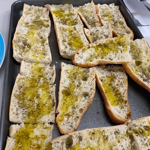 May include: A baking sheet filled with slices of bread brushed with olive oil and sprinkled with black pepper.