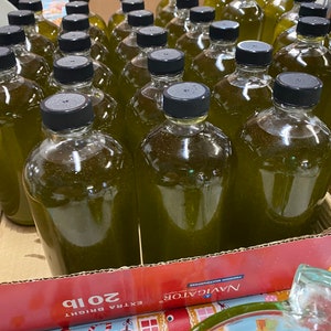 Puede incluir: Primer plano de una caja llena de numerosas botellas de vidrio de l&iacute;quido verde. Las botellas tienen tapas negras y est&aacute;n dispuestas en filas. La caja est&aacute; etiquetada con "Navigator Extra Bright 2018."