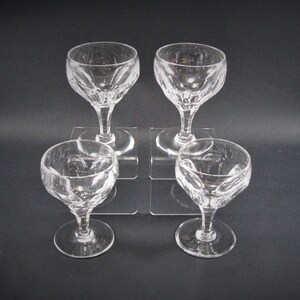 May include: Set of four clear glass stemmed drinking glasses with a cut glass design. The glasses are arranged on a white surface.