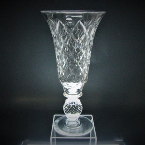 May include: A clear glass vase with a diamond pattern and a round base. The vase is on a clear glass pedestal.