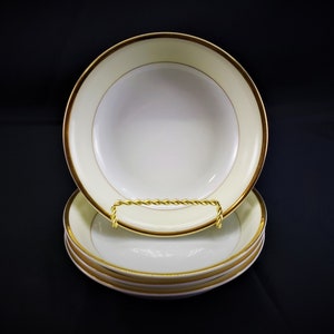 May include: Set of four white ceramic bowls with a gold rim. The bowls are stacked on top of each other.