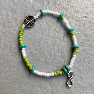 May include: White, green, and blue beaded bracelet with a silver spiral charm and an infinity symbol charm.