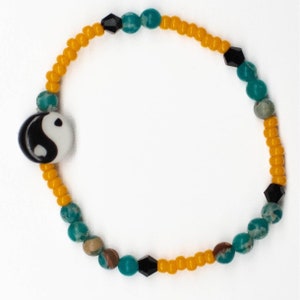 May include: A yellow, teal, and black beaded bracelet with a yin yang charm.