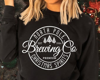 May include: Black sweatshirt with a white circle graphic that says "North Pole Brewing Co. Est. 1984 Premium Christmas Spirits" with a design of three pine trees inside the circle.