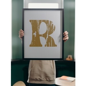 May include: A framed print of the letter "R" in a distressed gold font on a white background.
