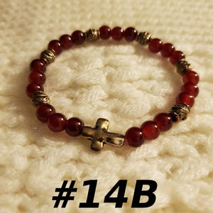 May include: Red gemstone bracelet with gold accents and a small gold cross charm. #14B