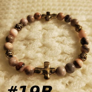 May include: A pink and grey stone bracelet with gold accents and two gold cross charms. The bracelet is labeled #19B.