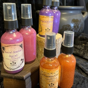 May include: Five glass bottles with spray tops and glitter inside. The bottles are labeled with different names and descriptions. The labels are in a gothic font and include the words "Amuk! Amuck!" "Amuk!" "A Calming Circle" and "BooOooOoK".