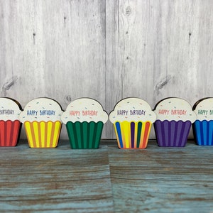 May include: Six wooden cupcake decorations with the words "Happy Birthday" on each. The cupcakes are in different colors: red, yellow, green, purple, blue, and orange.