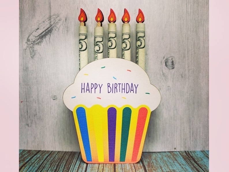 May include: A cupcake-shaped card with the words "Happy Birthday" on it. Five dollar bills are rolled up and inserted into the card to look like candles.