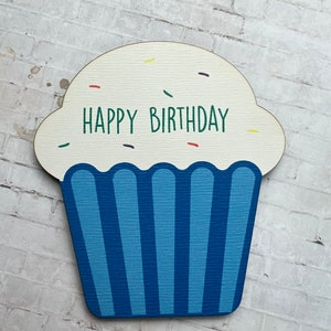May include: A wooden cupcake cutout with blue frosting and white sprinkles. The cupcake says "Happy Birthday" in green letters.