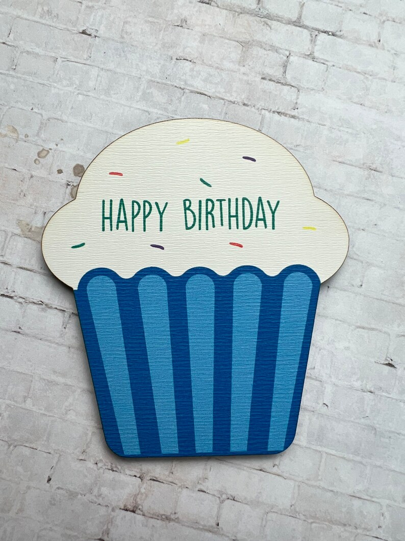 May include: A wooden cupcake cutout with blue frosting and white sprinkles. The cupcake says "Happy Birthday" in green letters.