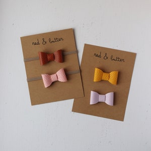 May include: Two sets of hair ties with bows. The first set has a brown bow, a pink bow, and the text "red & butter". The second set has a yellow bow, a light purple bow, and the text "red & butter".