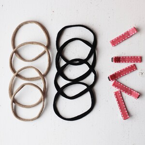 May include: A set of hair accessories including five brown hair ties, five black hair ties, and five red hair clips with white polka dots.