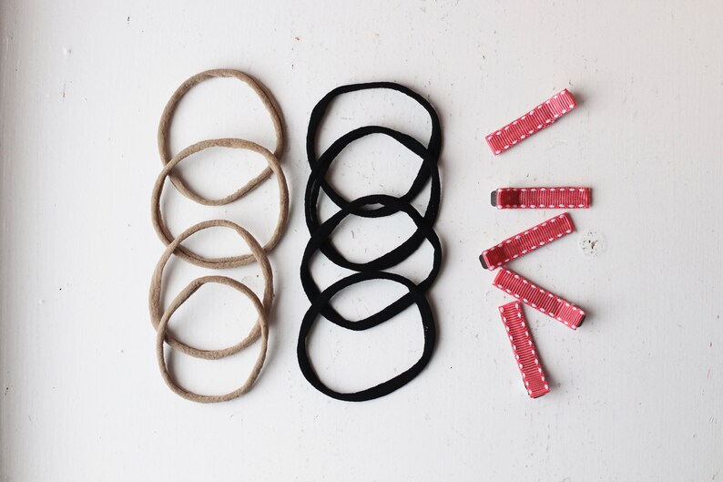 May include: A set of hair accessories including five brown hair ties, five black hair ties, and five red hair clips with white polka dots.