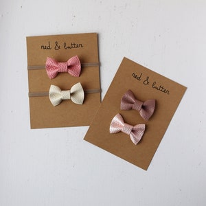 May include: Three sets of hair bows on brown cards. The bows are made of pink, white, and brown faux leather. The cards have the text "red & butter" printed on them.