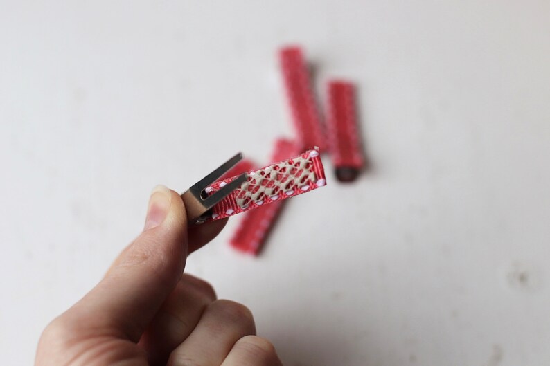 May include: A close-up of a red hair clip with white polka dots. The clip has a metal spring and a textured, beige fabric covering the top.