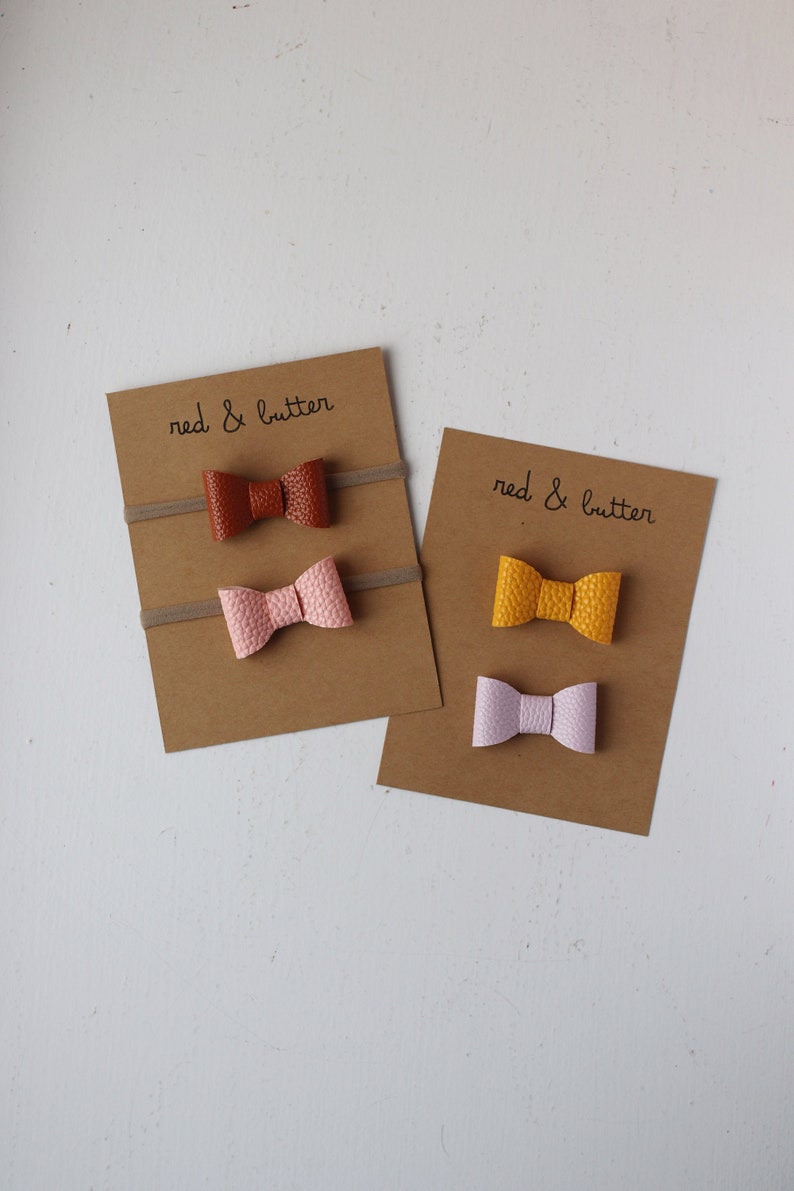 May include: Two sets of hair ties with bows. The first set has a brown bow, a pink bow, and the text "red & butter". The second set has a yellow bow, a light purple bow, and the text "red & butter".
