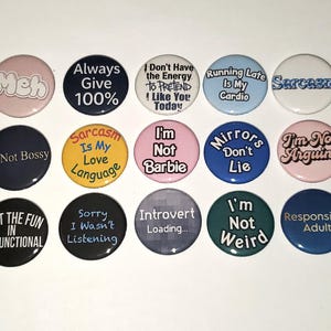 May include: A collection of round pinback buttons with various humorous phrases in white lettering on different colored backgrounds. The buttons include phrases like "Meh," "Sarcasm," and "I'm Not Weird."