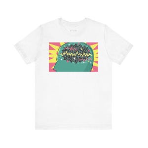 May include: White t-shirt with a graphic of a green head with a black and white brain inside. The brain is filled with colorful lines and stars. The graphic is surrounded by a yellow and red background with a white starburst.
