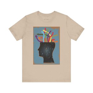May include: A beige t-shirt with a graphic of a head with colorful arrows coming out of it. The graphic is on a blue background with a brown border.