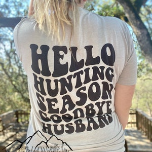 May include: A light gray t-shirt with a black graphic that says "Hello Hunting Season Goodbye Husband" in a retro font.