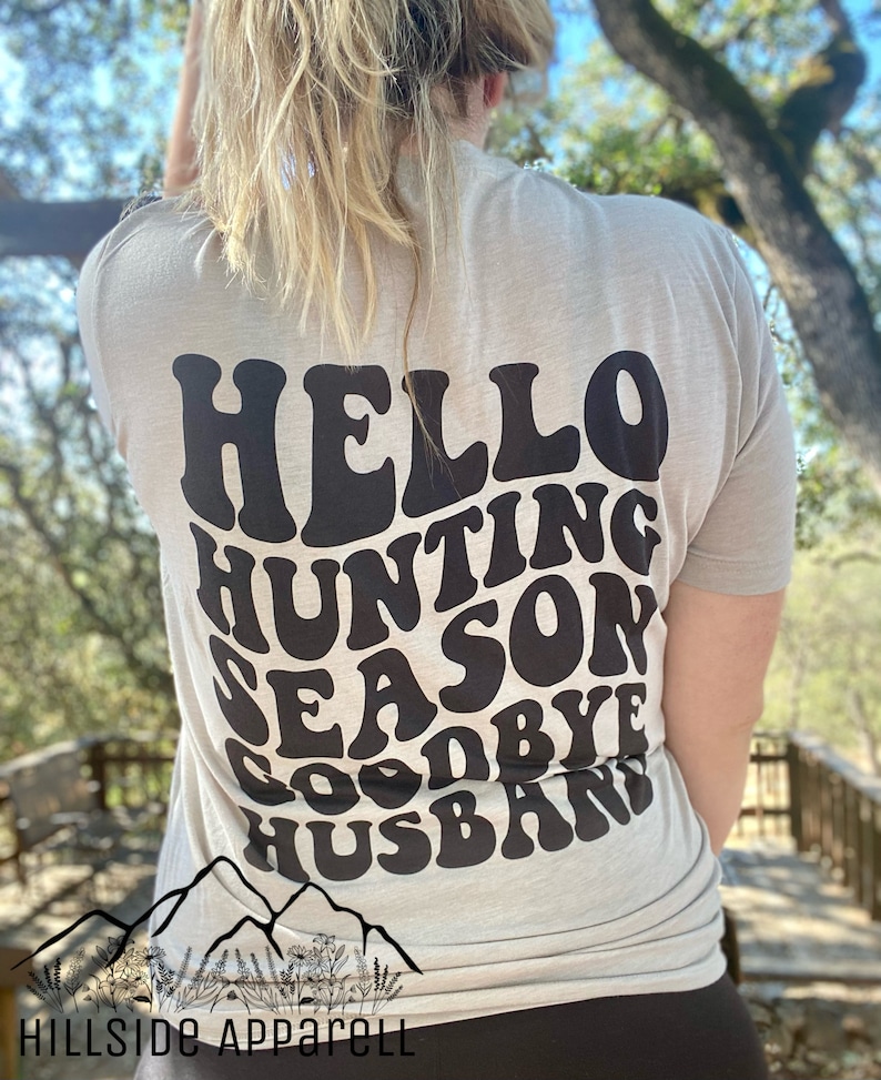 May include: A light gray t-shirt with a black graphic that says "Hello Hunting Season Goodbye Husband" in a retro font.