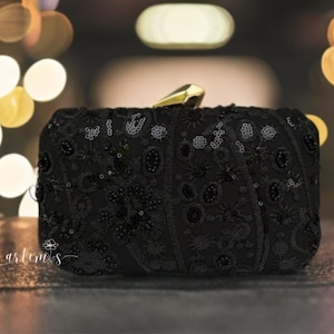 Puede incluir: Un clutch negro de lentejuelas con un cierre dorado. El clutch está decorado con un patrón floral.