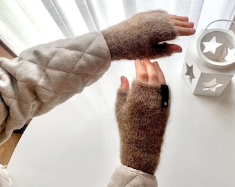 May include: A pair of brown fingerless gloves with a black button on one glove. The gloves are made of a soft, fuzzy material.