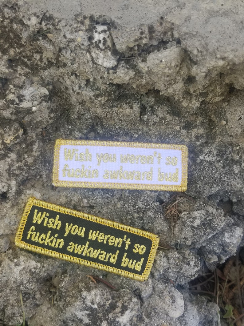 May include: Two embroidered patches with gold thread. The top patch is white with gold thread and says "Wish you weren't so fuckin awkward bud". The bottom patch is dark green with gold thread and says "Wish you weren't so fuckin awkward bud".