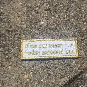 May include: White patch with gold stitching that reads "Wish you weren't so fuckin awkward bud".