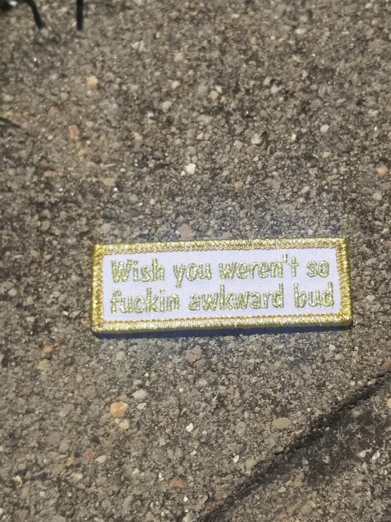May include: White patch with gold stitching that reads "Wish you weren't so fuckin awkward bud".