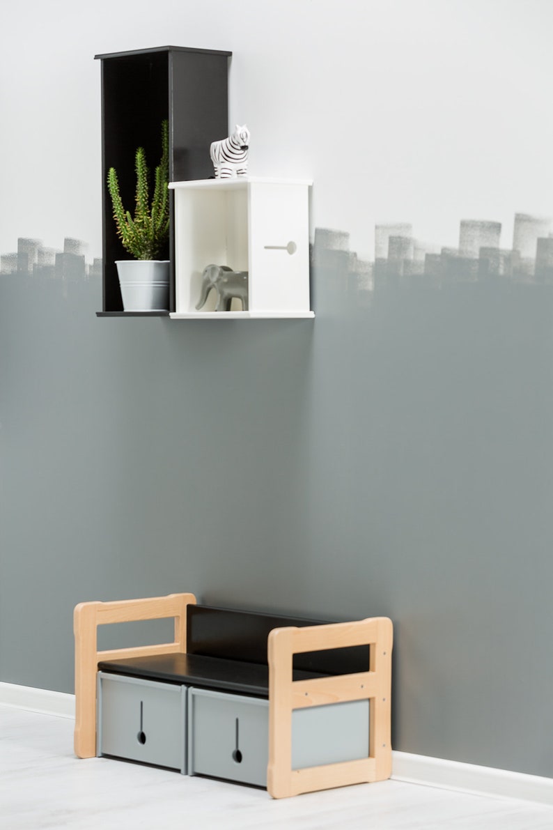May include: A black and white shelf unit with a potted cactus plant, a zebra figurine, and a grey elephant figurine. Below the shelf is a wooden storage bench with two drawers.