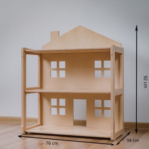 May include: A wooden dollhouse with a pitched roof and two levels. The dollhouse is 92 cm tall, 76 cm wide, and 34 cm deep.