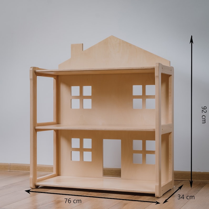 May include: A wooden dollhouse with a pitched roof and two levels. The dollhouse is 92 cm tall, 76 cm wide, and 34 cm deep.