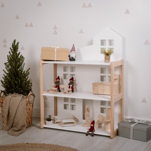 Puede incluir: Una casa de mu&ntilde;ecas de madera blanca de tres niveles, con muebles y accesorios en miniatura. La casa de mu&ntilde;ecas tiene una parte superior en forma de casa con ventanas. La escena incluye un peque&ntilde;o &aacute;rbol de Navidad, una caja de regalo y gnomos decorativos.